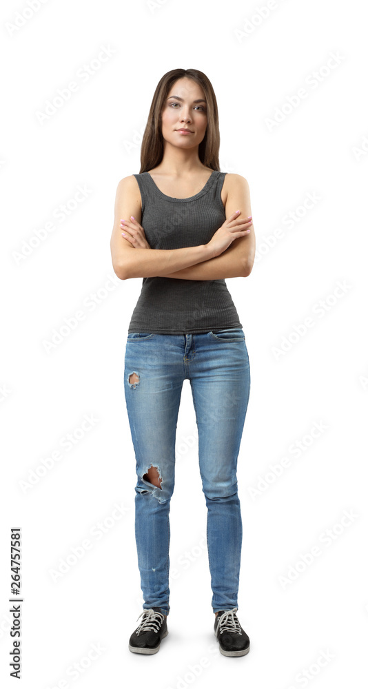 Φωτογραφία Front view of young attractive woman in gray sleeveless top and blue jeans standing with arms crossed on chest isolated on white background