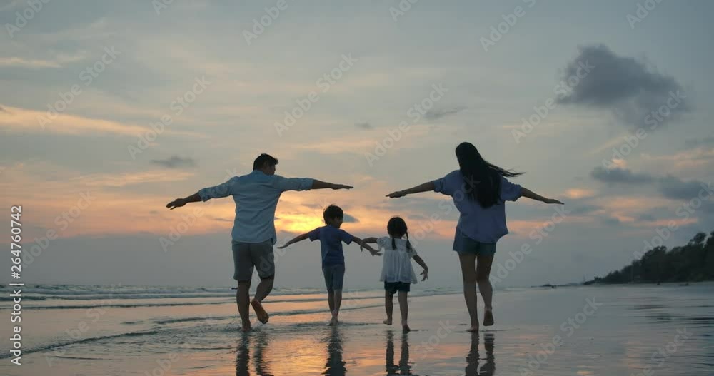 Silhouetted happy asian family playing and having fun on the beach at sunset. Slow Motion. Family, Freedom and Travel concept.