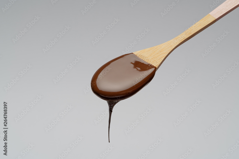 Liquid chocolate on a wooden spoon on light grey backgiund Liquid chocolate on a wooden spoon on light grey backgiund