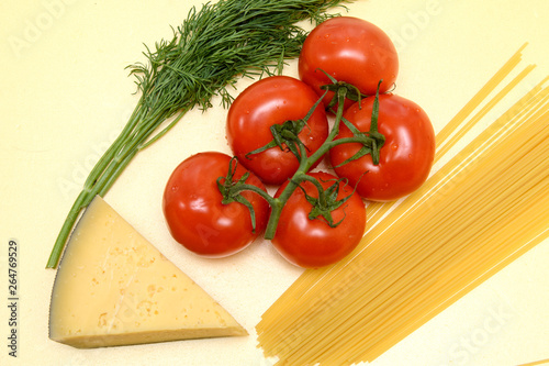On a yellow background, red tomatoes on a green branch, a slice of yellow cheese, spaghetti pasta, dill twigs. Concept - healthy food. Top view