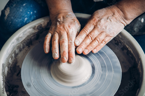 Wrinkled hands wizard on potter wheel makes clay dishes. Place to work