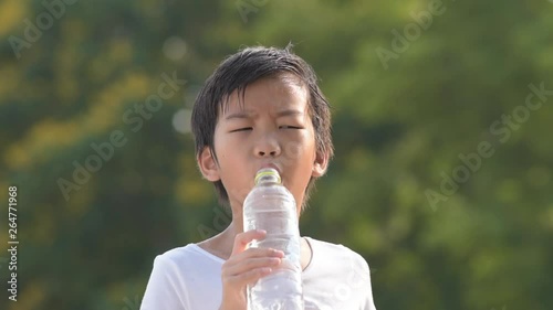 Young Asian boy got warm weather and drink water during summer day in a park