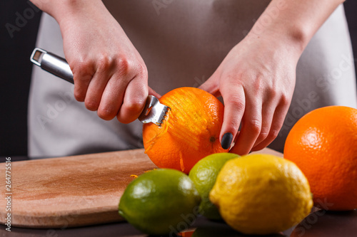 young woman in a gray aprons, cuts an orange zest