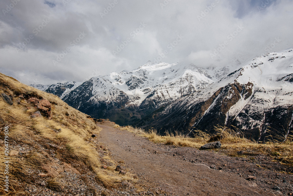 snow-capped mountains against a cloudy sky and a trail