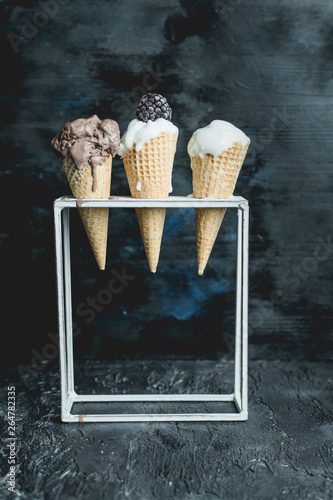 three ice cream in a wafer with frosted blackberrie on a metal stand, on a dark background photo