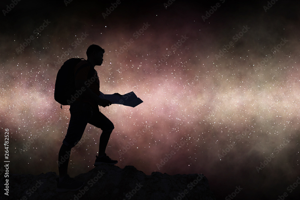 Silhouette travelling backpacker holding map on rocky mountain against milky way galaxy background