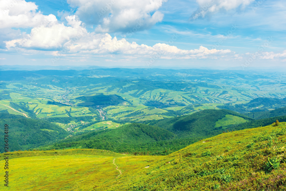 wonderful mountain landscape in summer.  green grassy hills and slopes. path downhill through the meadow. settlement and rural area in the distant valley. sunny weather with fluffy clouds on the sky