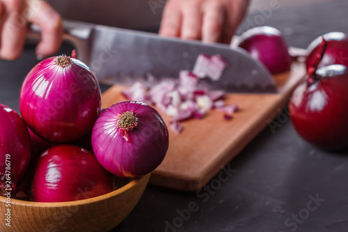 young woman in a gray aprons cuts red onion