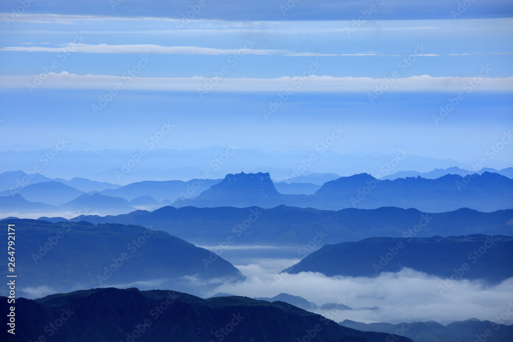 Abstract Image, Mountain Silhouettes at dawn - rolling jagged mountain peaks, cold blue color hues. Panoramic Abstract Background Image, overcast skies, layers of rolling mountains in the distance.