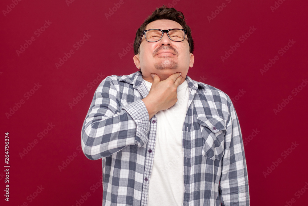 Throat pain on cold. Portrait of middle aged man in casual checkered shirt and eyeglasses standing and holding his painful neck because his sick