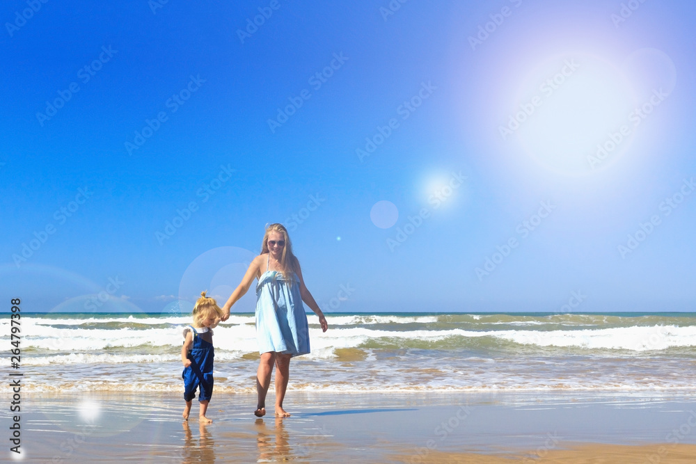Mom and daughter are walking on the beach. Front view, copy space.