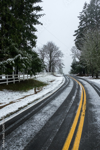 A lightly snow covered road just outside Portland, Oregon, USA, the double yellow lines leading off into the distance, no traffic