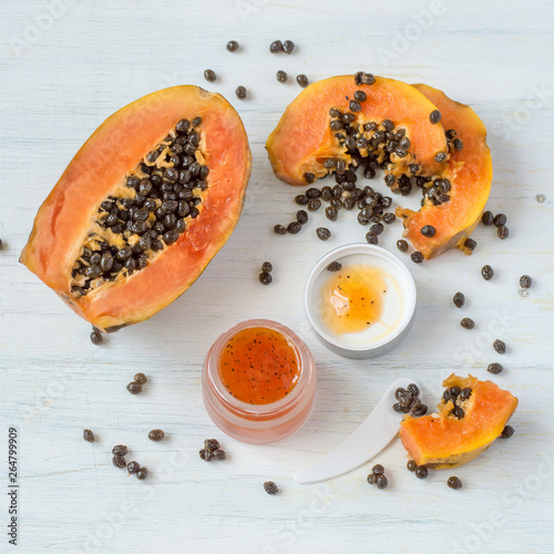 A small glass jar with a cosmetic face mask based on papaya fruit on a light wooden background. Selective focus.