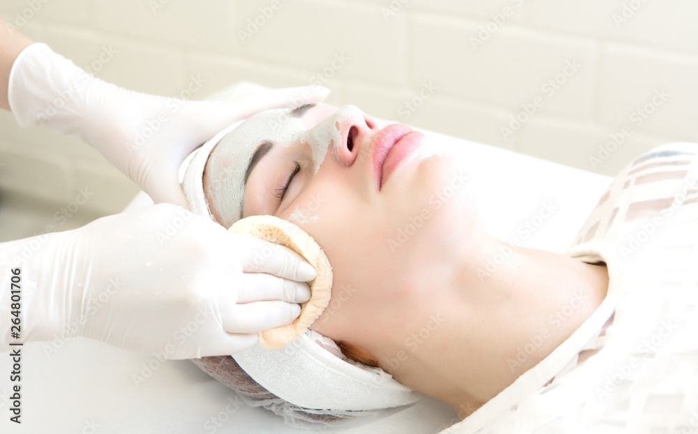 a girl in a white sterile hat lies on a couch with a beautician and she is given a mask and skin care