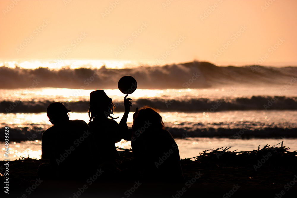 Silhouette of young friends playing with a ball on the beach on sunset