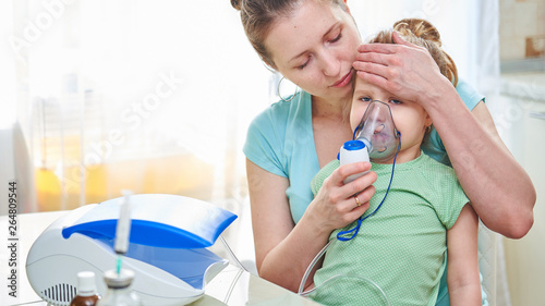 medicine on the table. the woman holds the child, checks the temperature by applying a palm to the child's head. I feel bad because of the disease. the girl breathes through a nebulizer mask