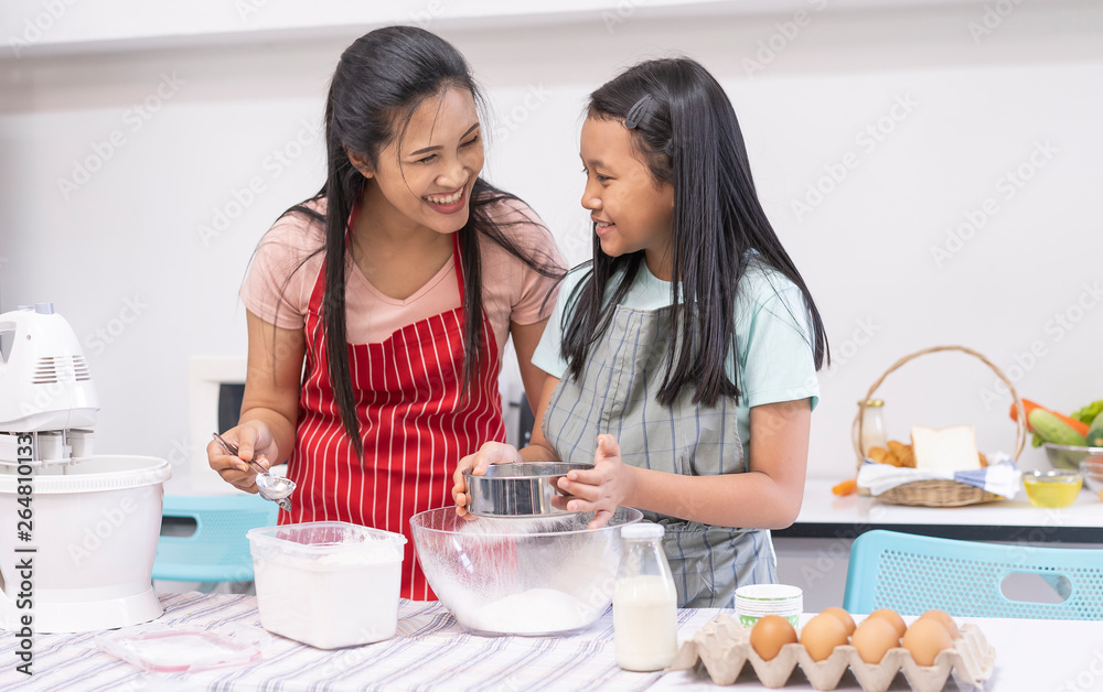 Young Asian family cooking food in kitchen. Happy teenage girl with her mother mixing batter in the bowl together. good team,Time of happiness. vacation holiday and Cooking together concept Young Asian family cooking food in kitchen. Happy teenage girl with her mother mixing batter in the bowl together. good team,Time of happiness. vacation holiday and Cooking together concept