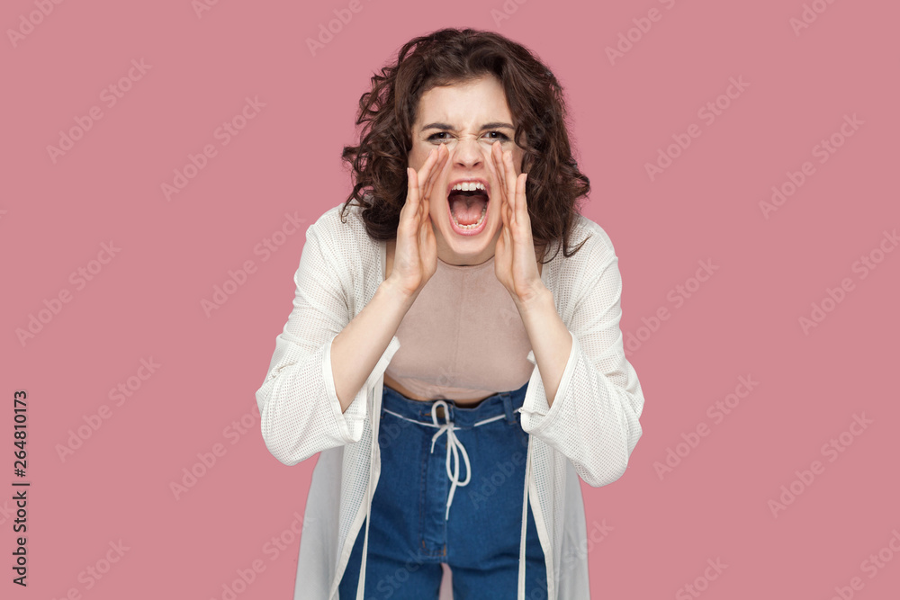 Portrait of beautiful brunette young woman with curly hairstyle in casual style standing, looking at camera and screaming. people expression and emotion. indoor studio shot isolated on pink background Portrait of beautiful brunette young woman with curly hairstyle in casual style standing, looking at camera and screaming. people expression and emotion. indoor studio shot isolated on pink background