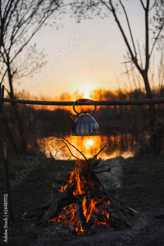 Fototapeta Naklejka Na Ścianę i Meble -  Teapot on the fire prepares tea. Orange sunset