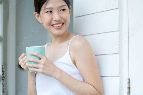 beautiful asian teen white Tank top happiness smile enjoy freshness morning with hot drink near window with sun light