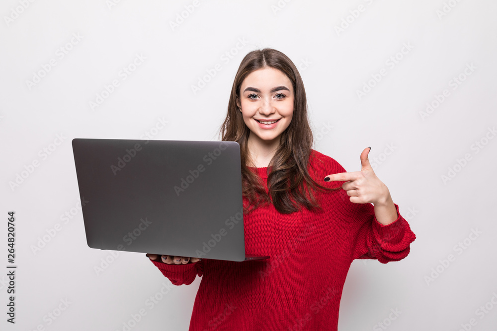 Smiling young woman holding and pointing on laptop over grey background Smiling young woman holding and pointing on laptop over grey background