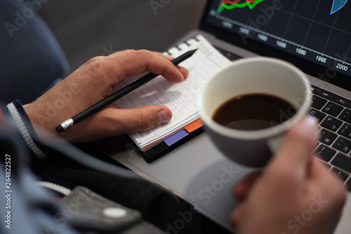 Young businessman analysing finance statistic on laptop with cup coffee in hand.