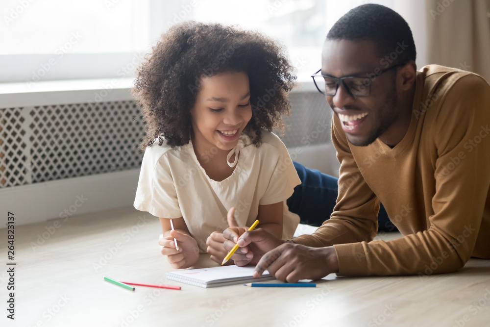 African father drawing with little daughter lying on heated floor African father drawing with little daughter lying on heated floor