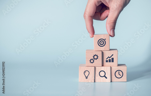 Woman hand arranging wood block with icon business strategy and Action plan, copy space.