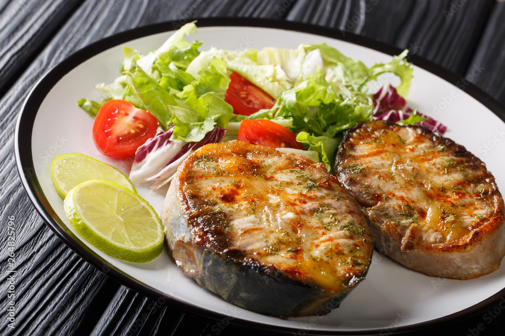 Tender fried sturgeon steaks served with fresh vegetable salad close-up on a plate. horizontal