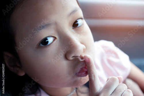 Fotografie Closeup portrait secretive asian child girl placing finger keep quiet gesture
