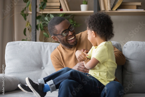 African father tickling little adorable son having fun at home