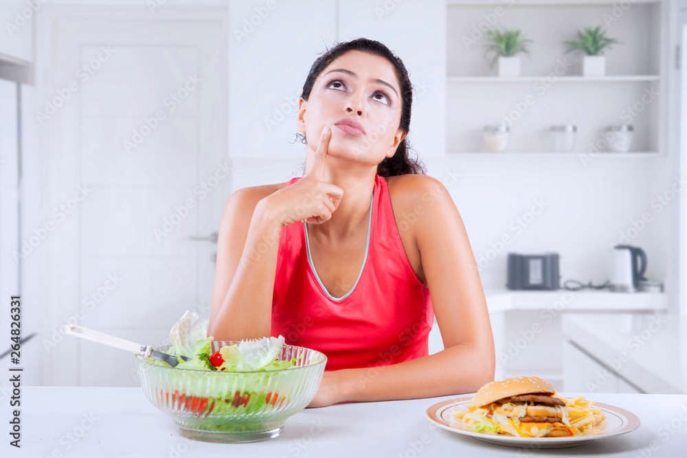 Young woman thinks to choose burger or salad Young woman thinks to choose burger or salad