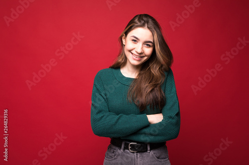 Portrait of pensive young woman in green sweater holding hands crossed, looking aside isolated on bright red background