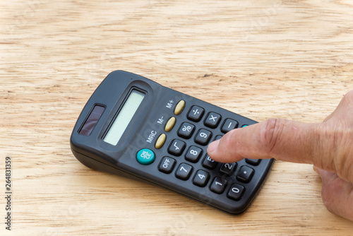 person making account, in a pocket calculator with a wooden background.