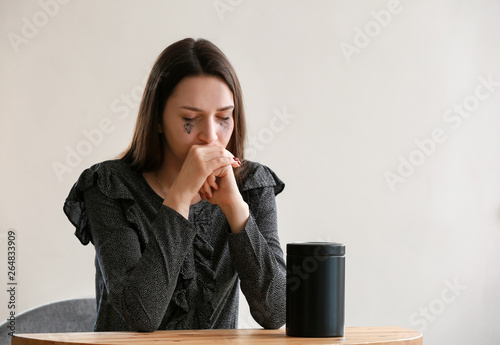 Sad woman with mortuary urn sitting at table
