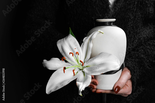 Obraz na plátně Woman holding mortuary urn with lily flower, closeup