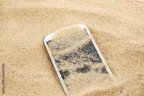 White smartphone lost in sand on the beach