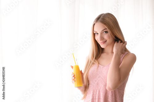 Beautiful young woman with fresh juice near window