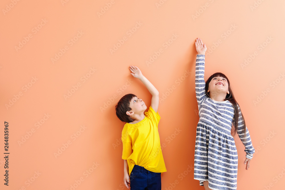 Cute little children measuring height near color wall - obrazy, fototapety, plakaty 