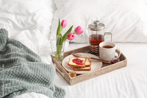 Tray with tasty breakfast and flowers on bed