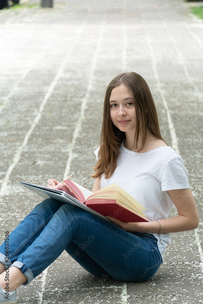 Obraz premium Teenage girl studying sitting on the walkway, outdoors