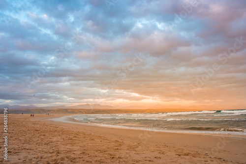 Rays of golden evening light falling on the Plettenberg Bay beach at sunset, with mountains in the distance. Garden Route, Western Cape, South Africa