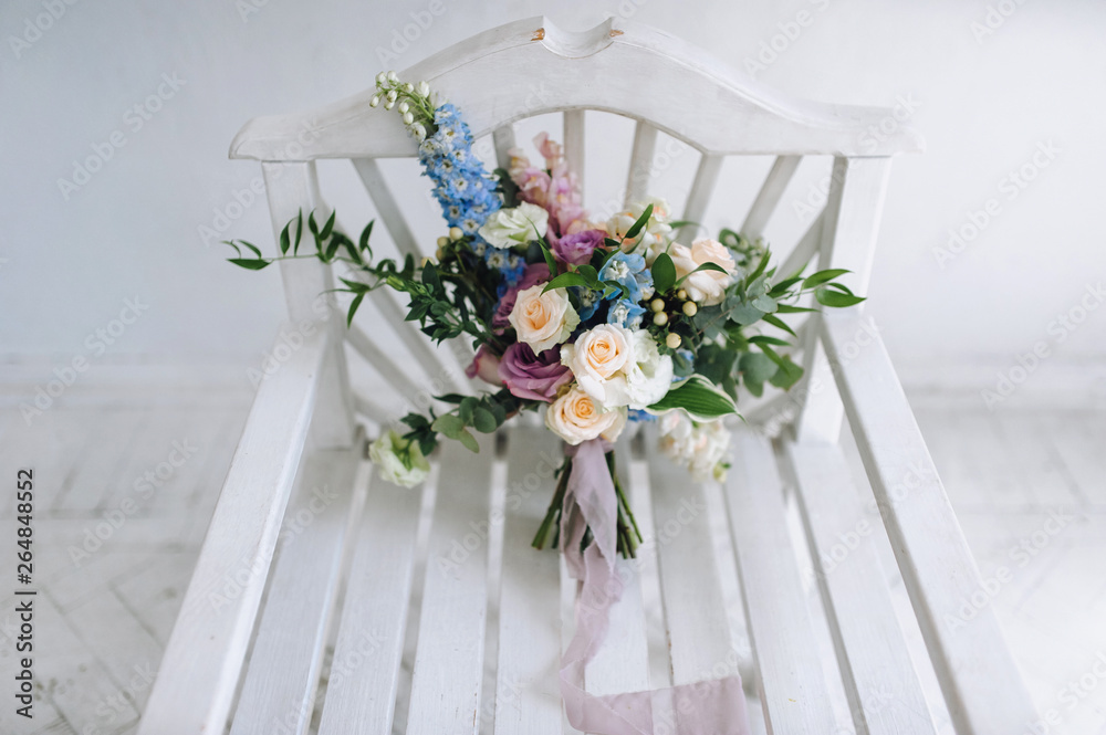 Beautiful and stylish wedding bouquet with roses closeup lies on a white wooden chair in a modern studio. Wedding details and decorations.