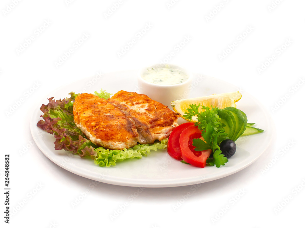 Fried sturgeon on lettuce leaves with fresh vegetables, parsley leaves, a slice of lemon and olive on a plate