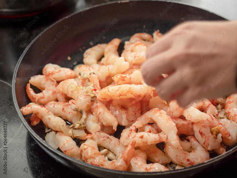 Frying pan with prawns, cook adds spices and herbs. Frying pan with prawns, cook adds spices and herbs.