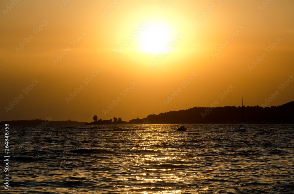 beautiful sunset over beach of Toroni, Sithonia, Halkidiki, Greece,  with some boats on sea and hill as silhouette