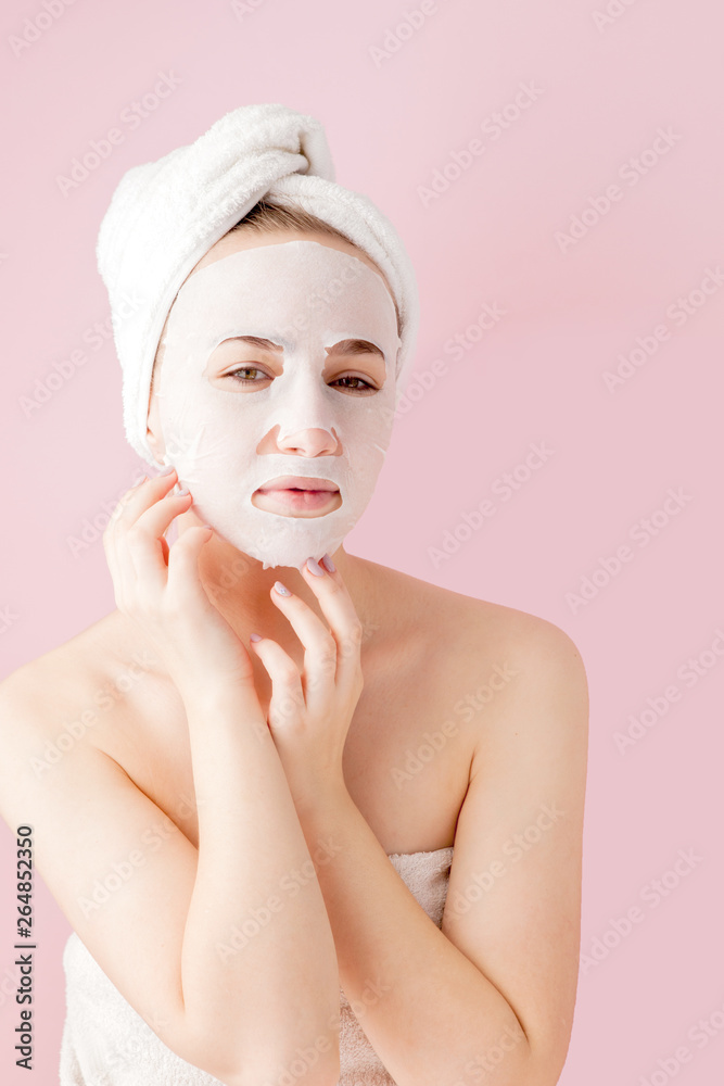 Beautiful young woman is applying a cosmetic tissue mask on a face on a pink background. Healthcare and beauty treatment and technology concept Beautiful young woman is applying a cosmetic tissue mask on a face on a pink background. Healthcare and beauty treatment and technology concept