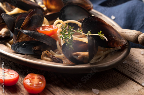 close up of golden plate with italian pasta and mussels, cut tomatoes and rosemary on wooden background