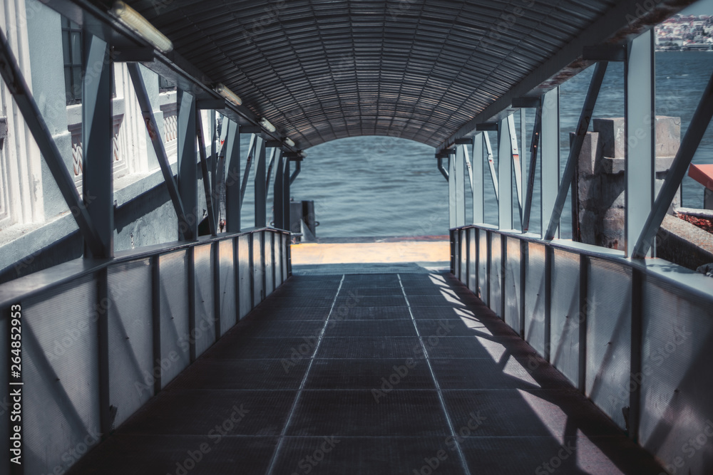 Descending boarding gate covered corridor with plenty of beams, on the quay for passengers of a boat or a ship, with river water in the background, selective focus in a middle, shallow depth of field Descending boarding gate covered corridor with plenty of beams, on the quay for passengers of a boat or a ship, with river water in the background, selective focus in a middle, shallow depth of field