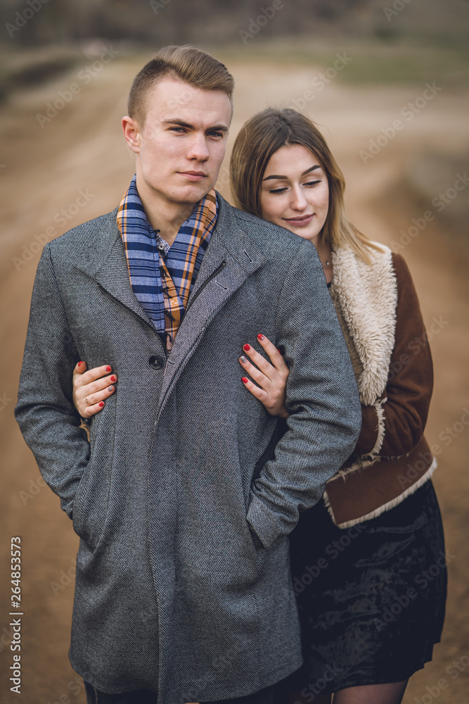 A nice beautiful lovely couple in the park or field. man in Gray coat and scarf with girl woman in brown coat. lovers walking hold hands. put her head on his shoulder hugged behind A nice beautiful lovely couple in the park or field. man in Gray coat and scarf with girl woman in brown coat. lovers walking hold hands. put her head on his shoulder hugged behind